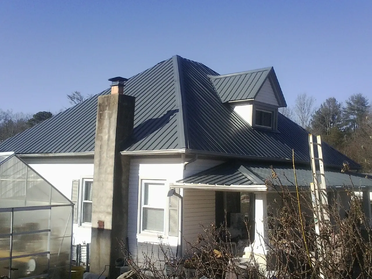 Dark blue standing seam metal roof on a white farmhouse with dormer — Slate & Tile Roof Repair by Roofing Brothers in Myrtle