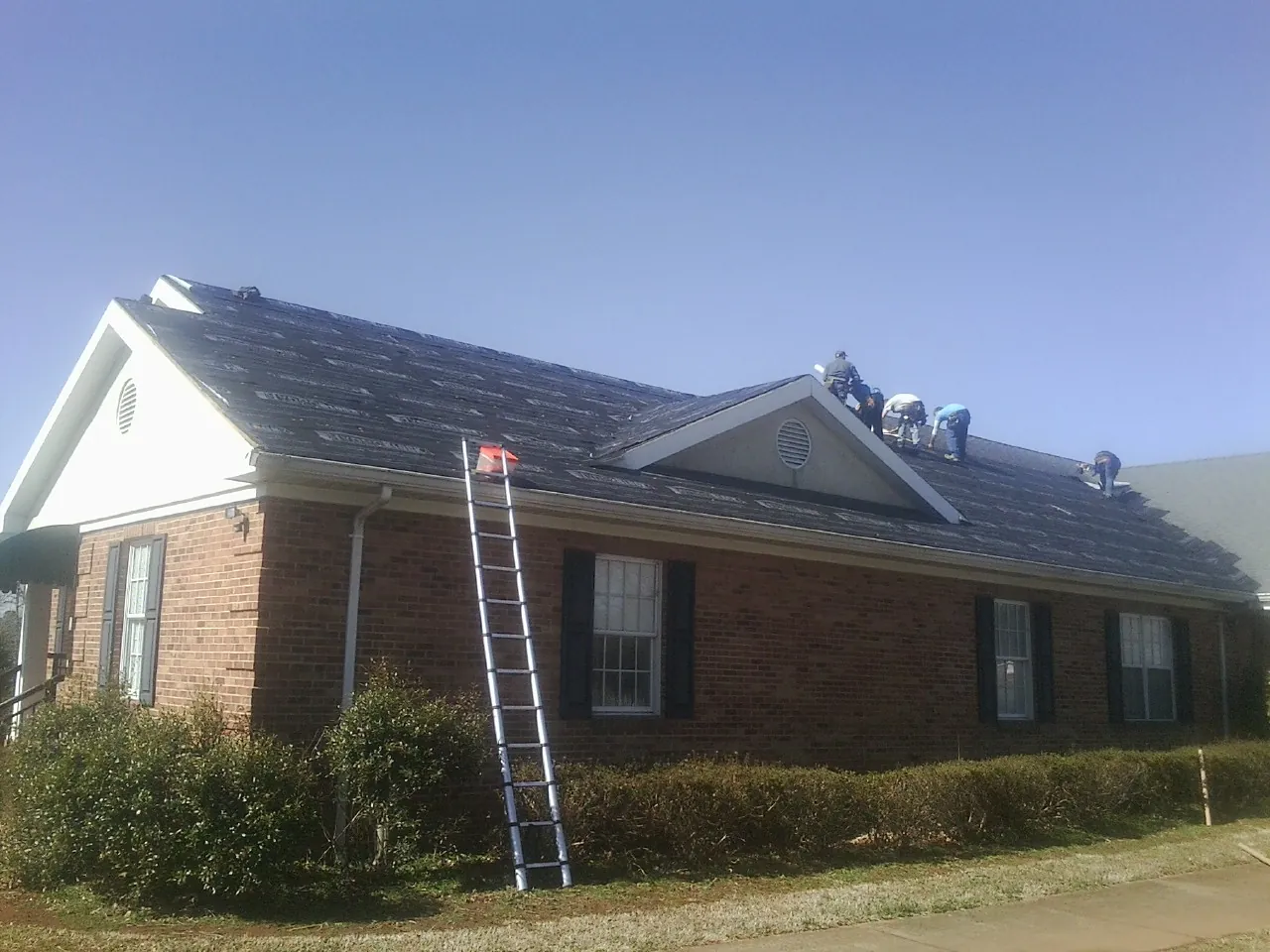 Crew tearing shingles off a brick ranch roof with a ladder set — Metal Roof Repair work by our crew in Myrtle