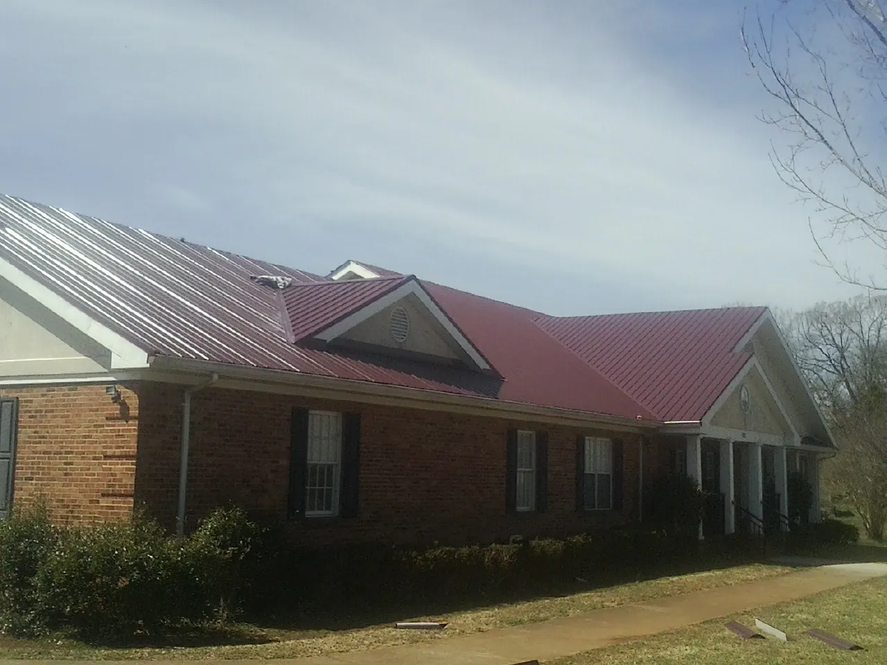 Red metal roof with gabled entries on a long brick building, from a Hail Damage Roof Repair job in Myrtle
