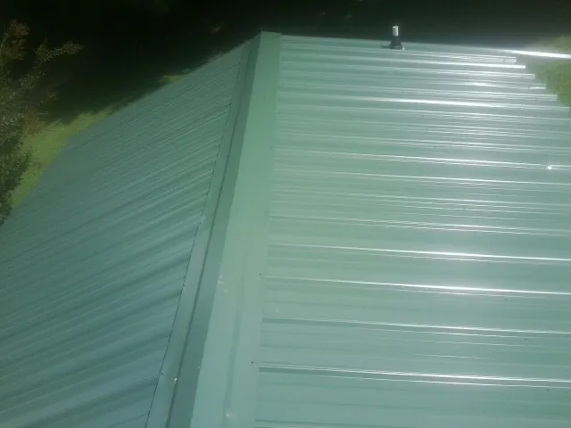 New green metal panels meeting at the ridge of a roof — Flat Roof Repair work by our crew in Myrtle