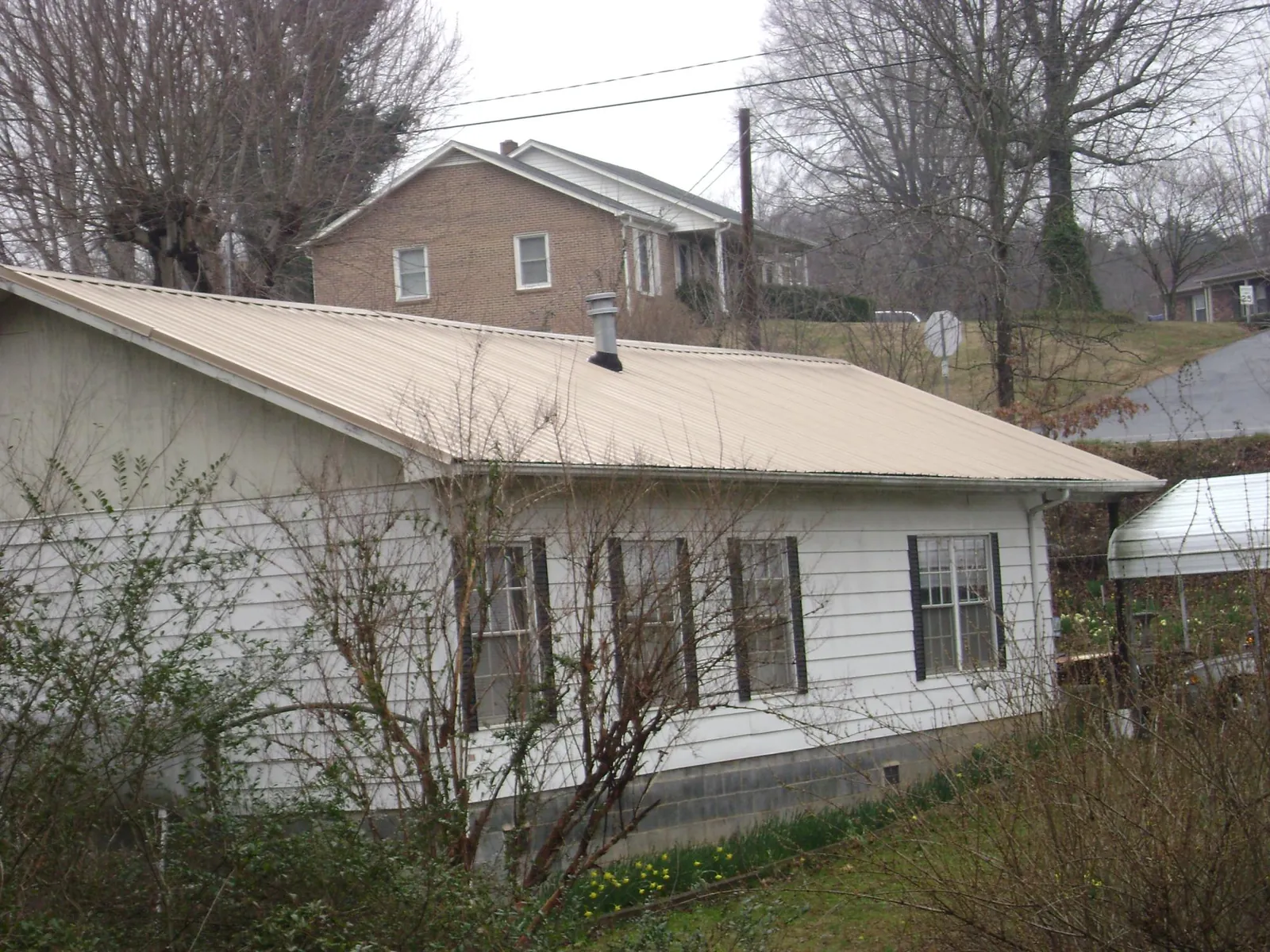 Tan metal roof on a white sided house set into a hillside — Commercial Roofing by Roofing Brothers in Myrtle