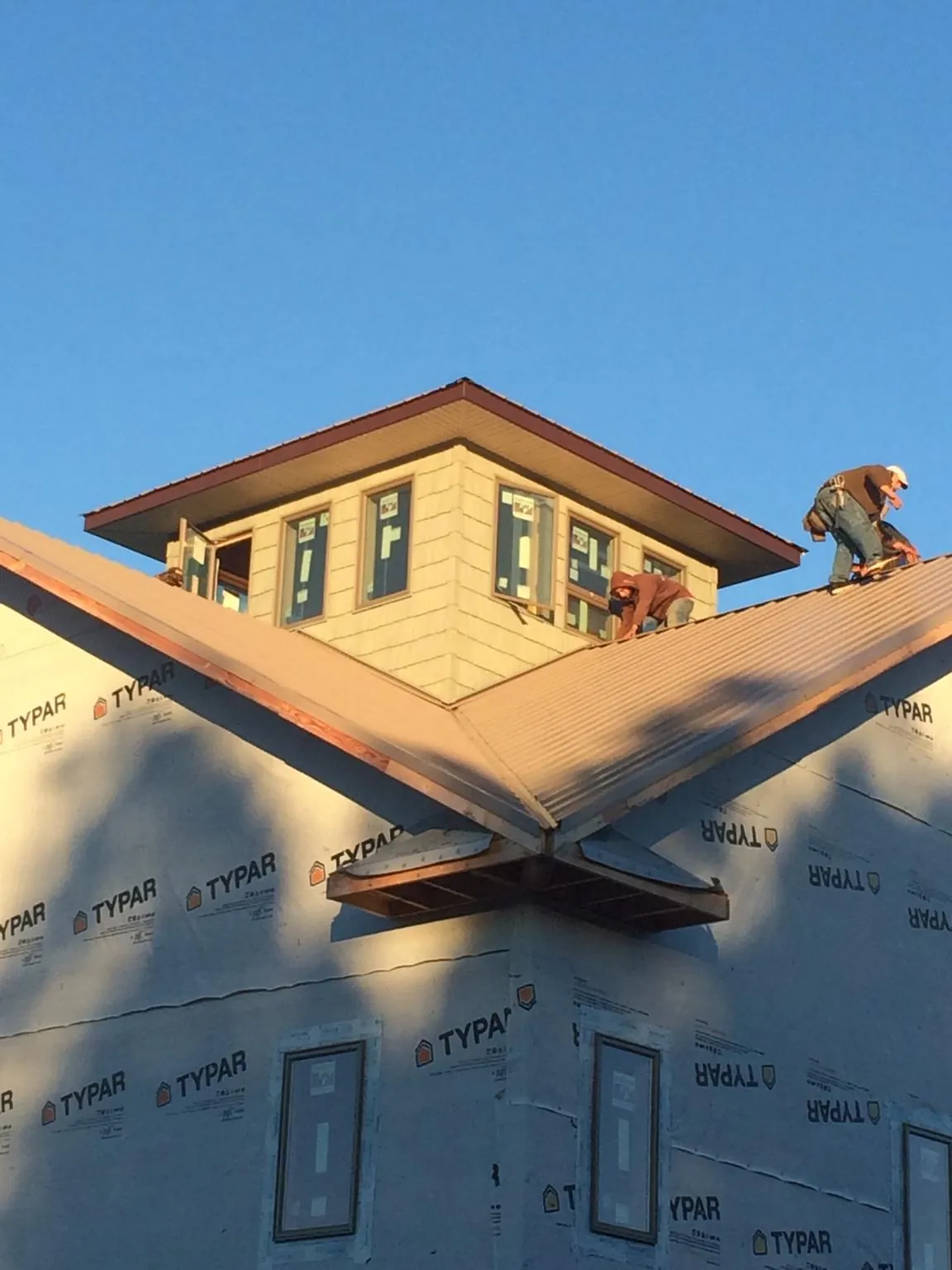 Roofers working around a rooftop cupola on a new metal roof at sunset — Roof Waterproofing in Myrtle by Roofing Brothers